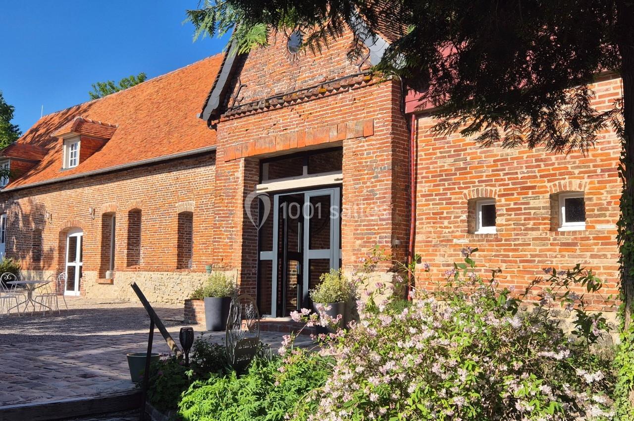 Façade en briques rouges d'un bâtiment ancien avec des fleurs et une cour pavée sous un ciel bleu.