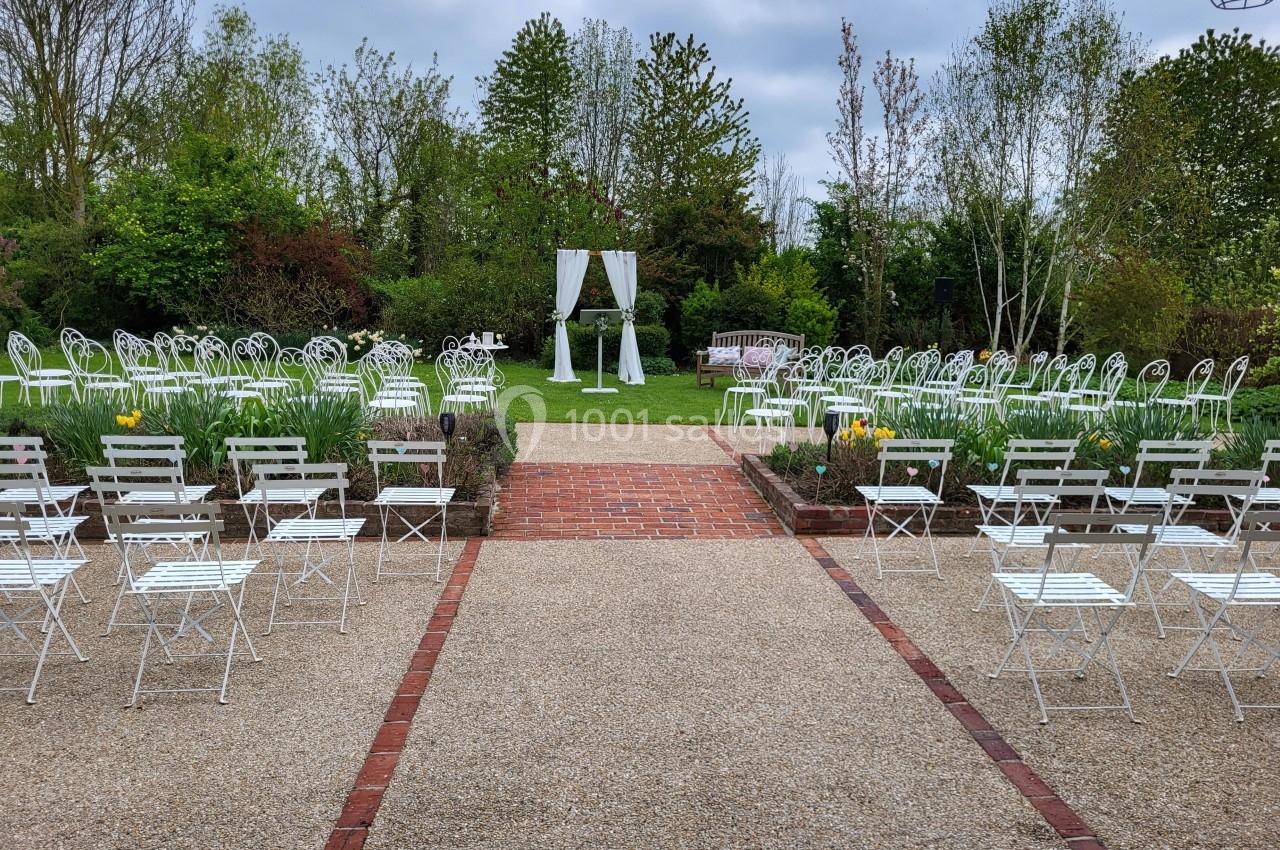 Allée centrale menant à une arche blanche entourée de chaises disposées pour une cérémonie en extérieur.