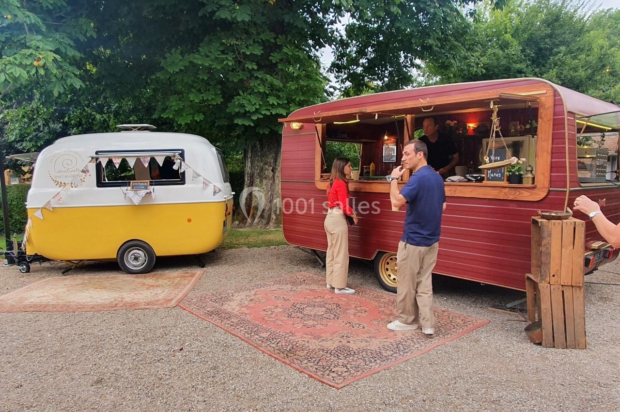Deux caravanes aménagées en stands de restauration, avec des clients dans une cour extérieure arborée.