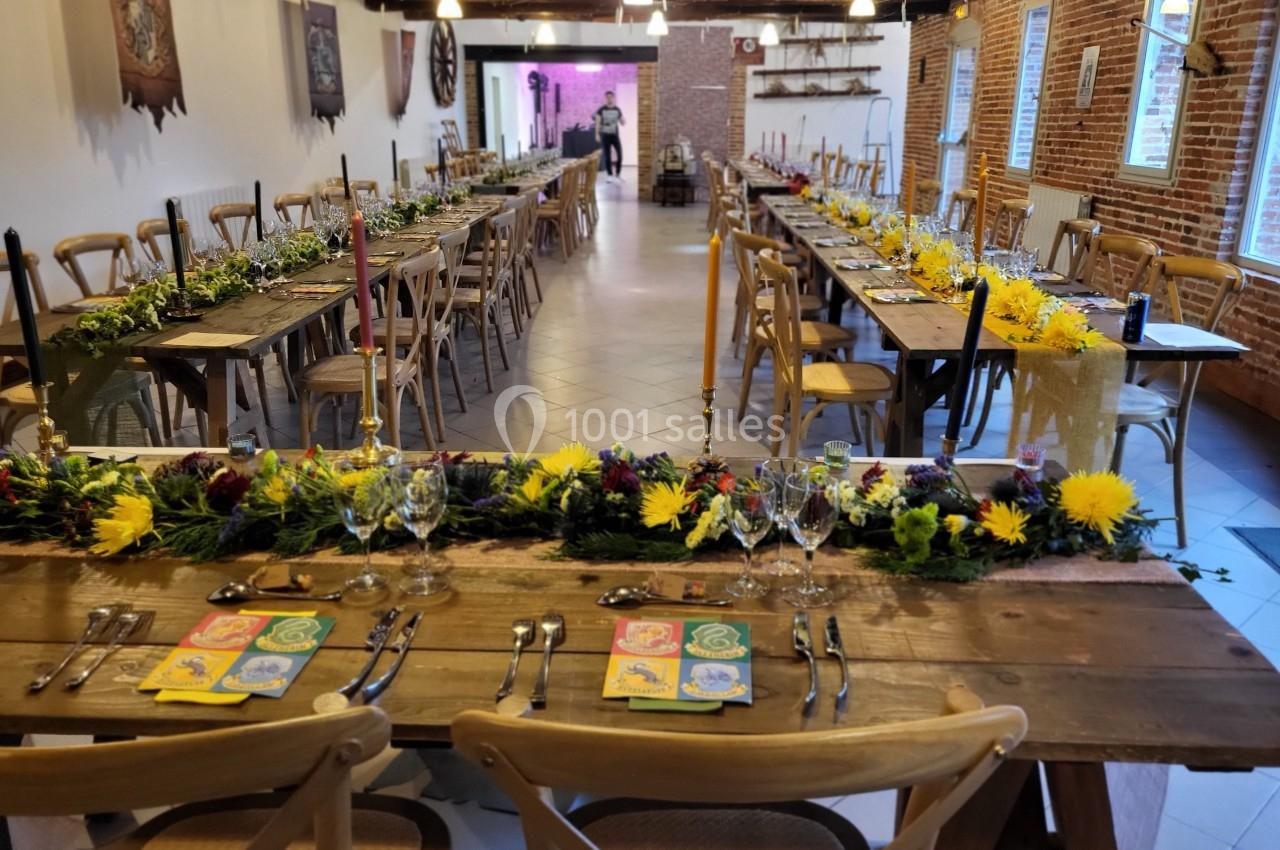 Salle de réception décorée avec des tables en bois, des fleurs jaunes et des bougies, prête pour un événement.