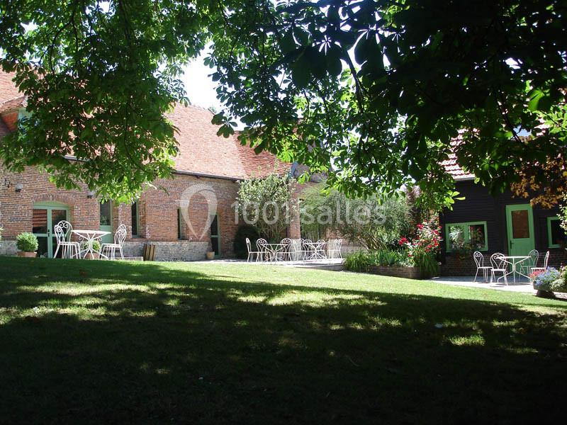 Cour verdoyante avec tables et chaises en fer forgé, entourée de bâtiments en briques sous un ciel dégagé.