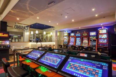 Salle de casino avec machines à sous lumineuses, écrans de jeux interactifs et un bar en arrière-plan.