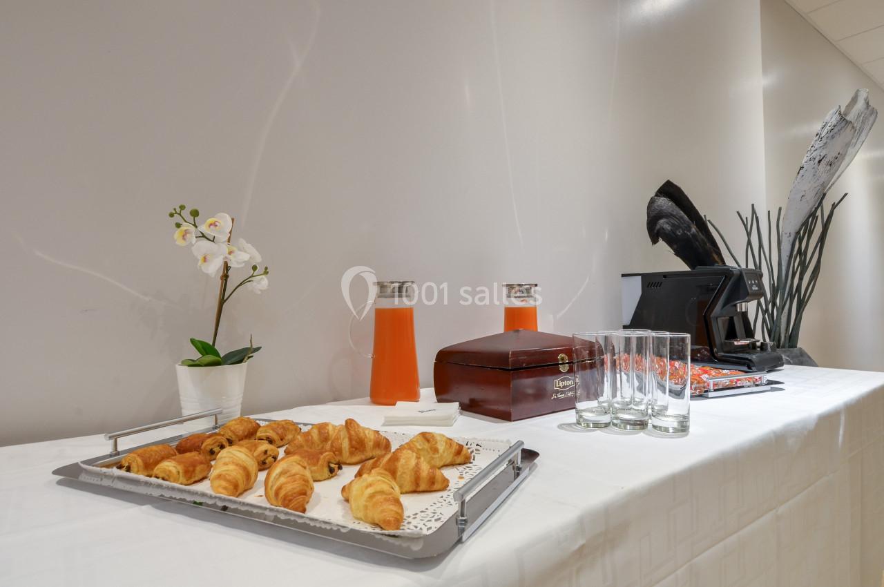 Plateau de croissants, carafes de jus d'orange, verres et orchidée blanche sur une table dressée.