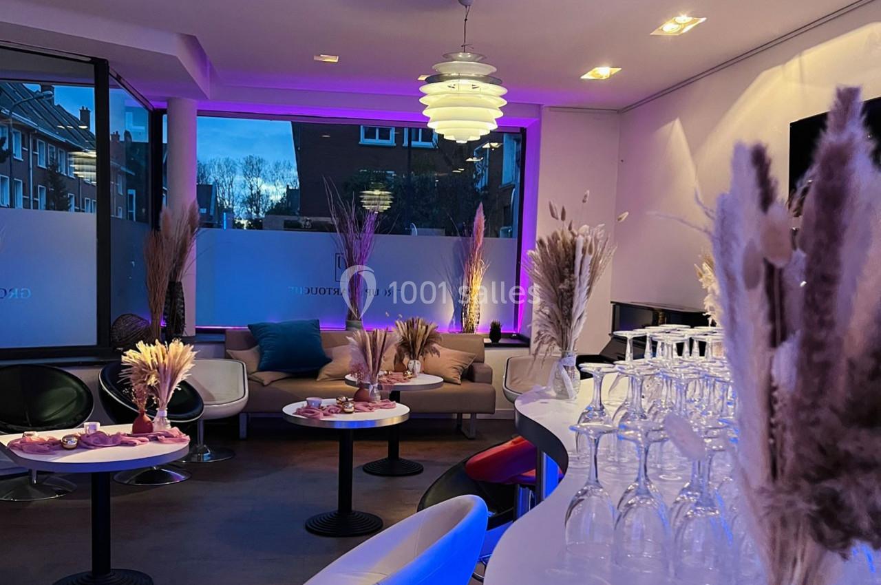 Salle moderne avec tables décorées de bouquets de fleurs séchées, éclairage tamisé et grandes baies vitrées donnant sur l…