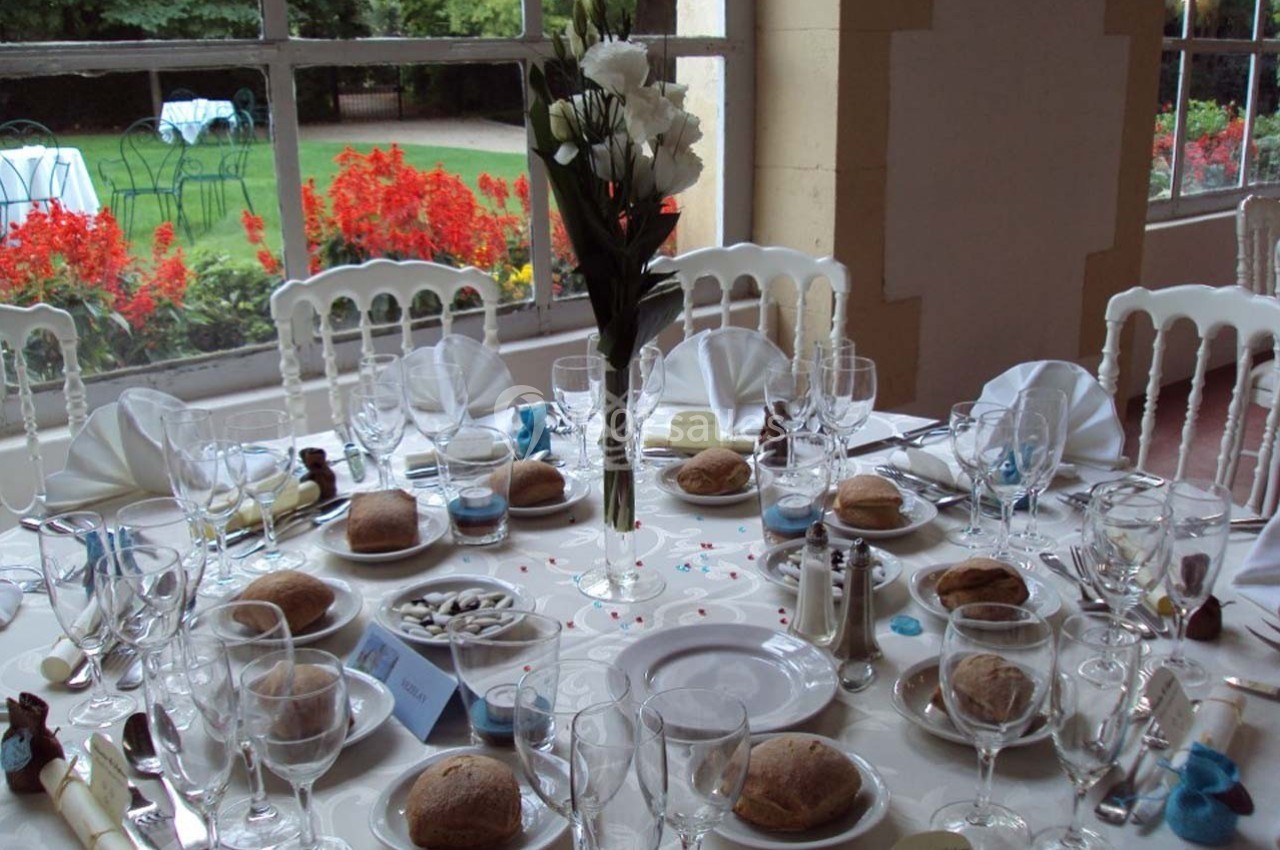 Table élégamment dressée avec vaisselle, pain et décorations florales, donnant sur un jardin fleuri à travers une baie…