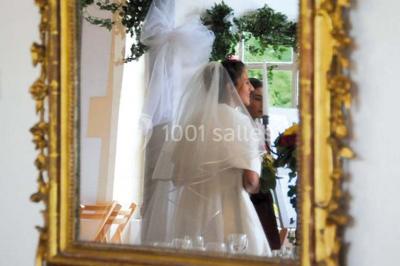 Un couple en tenue de cérémonie est transporté dans une calèche tirée par des chevaux sur un chemin bordé d'arbres.
