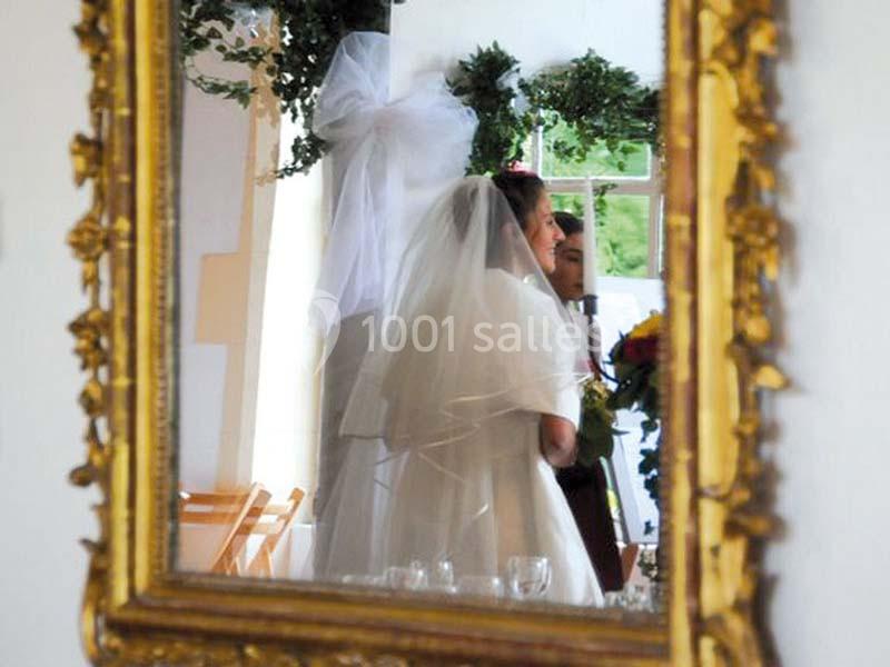 Reflet d'une mariée en robe blanche et voile dans un miroir doré, avec un décor floral en arrière-plan.