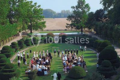 Un couple en tenue de cérémonie est transporté dans une calèche tirée par des chevaux sur un chemin bordé d'arbres.