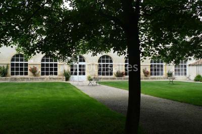 Un couple en tenue de cérémonie est transporté dans une calèche tirée par des chevaux sur un chemin bordé d'arbres.