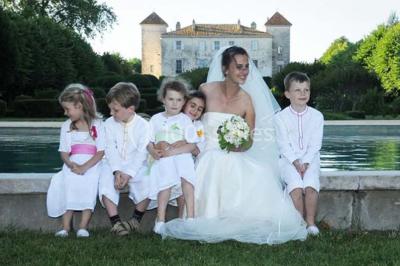 Un couple en tenue de cérémonie est transporté dans une calèche tirée par des chevaux sur un chemin bordé d'arbres.