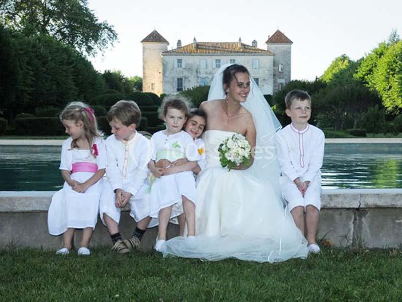 Une mariée souriante assise près d'un bassin, entourée de jeunes enfants en tenue blanche devant un château.