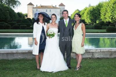 Un couple en tenue de cérémonie est transporté dans une calèche tirée par des chevaux sur un chemin bordé d'arbres.