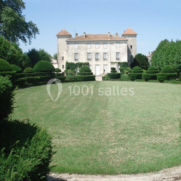 Château ancien entouré de jardins arborés et d'une pelouse bien entretenue sous un ciel dégagé.