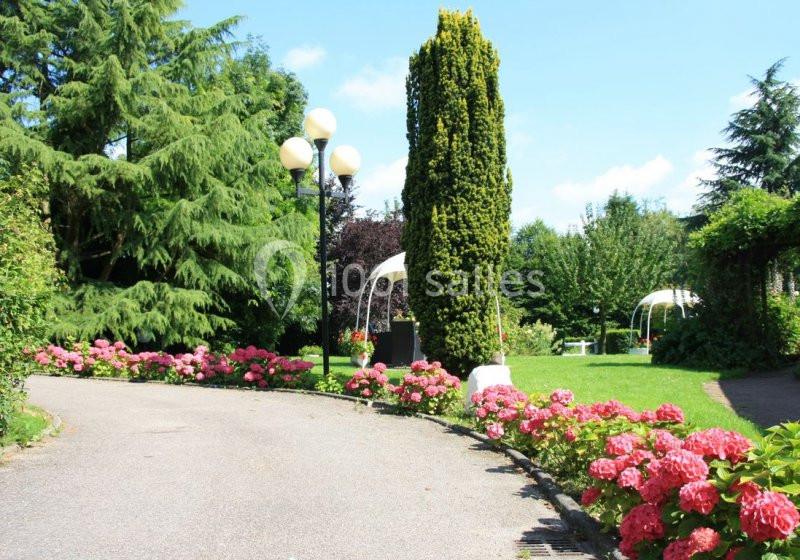 Allée bordée d'hortensias roses menant à un jardin verdoyant avec des arbres et des structures blanches.