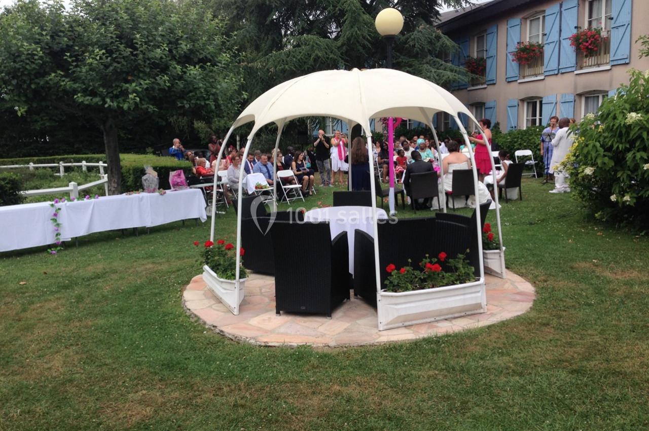 Groupe de personnes réunies dans un jardin avec tables, chaises et une tonnelle blanche au premier plan.