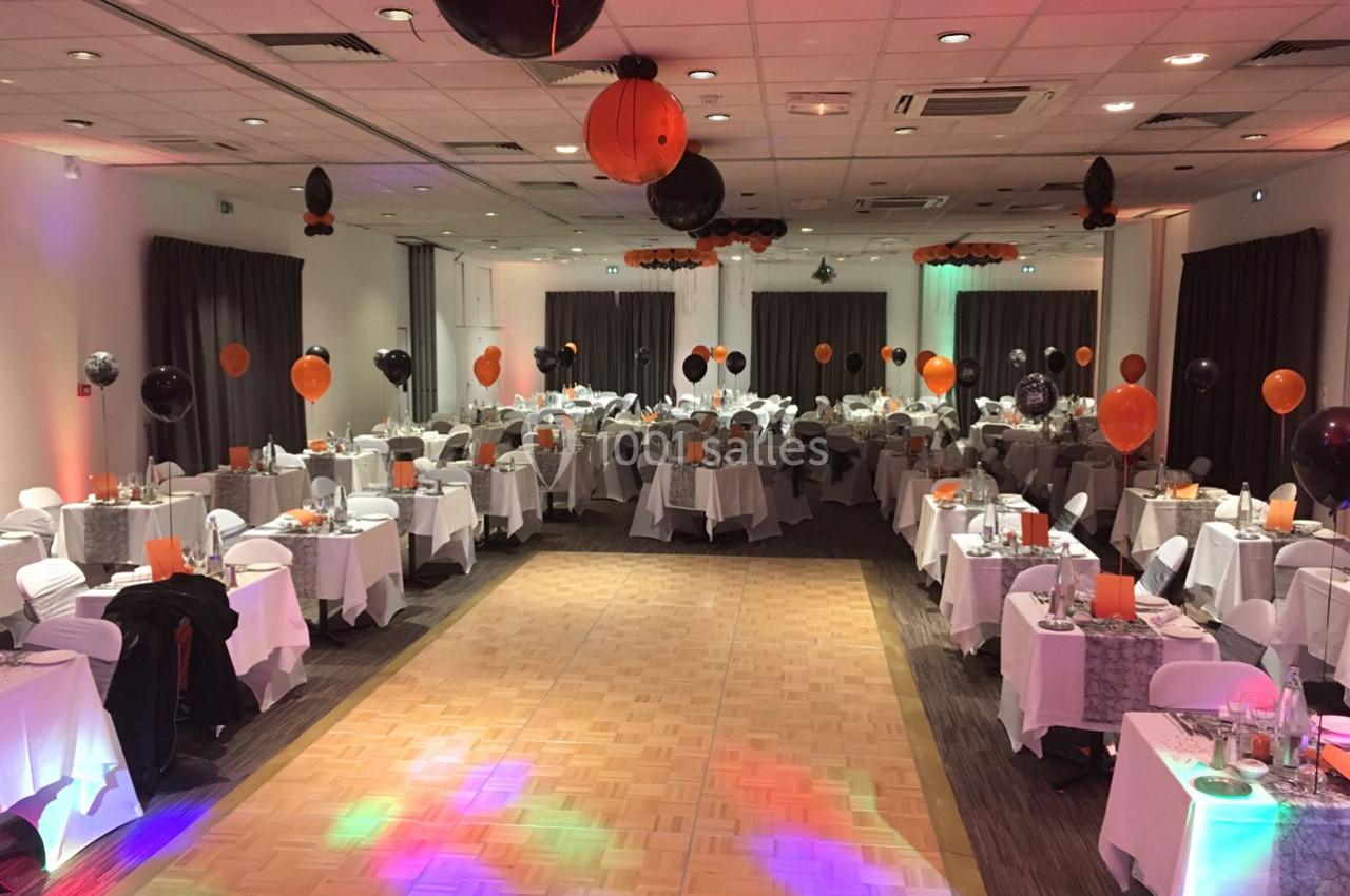 Salle de réception décorée avec des ballons noirs et orange, tables dressées pour un événement festif.