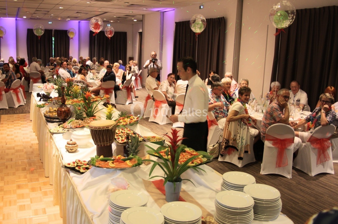 Salle de réception avec invités assis, buffet garni au premier plan et serveur en mouvement.