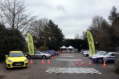 Plusieurs motos garées en ligne dans un parking extérieur bordé de haies et d'arbres.