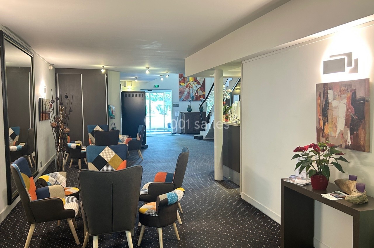 Espace d'accueil lumineux avec fauteuils colorés, table basse, miroir et comptoir près d'une entrée vitrée.
