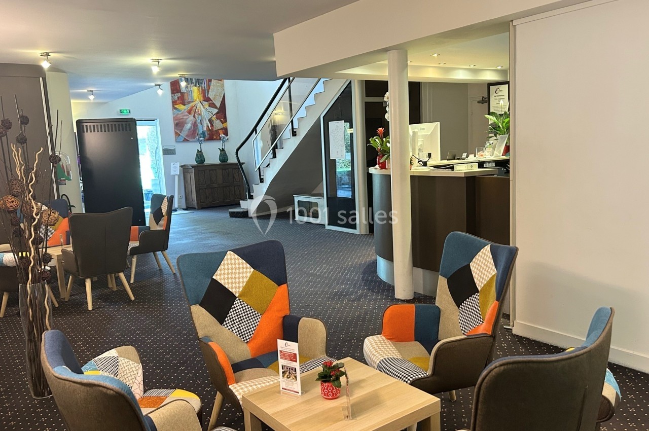 Espace d'accueil lumineux avec des fauteuils colorés, une table basse et un comptoir de réception en arrière-plan.