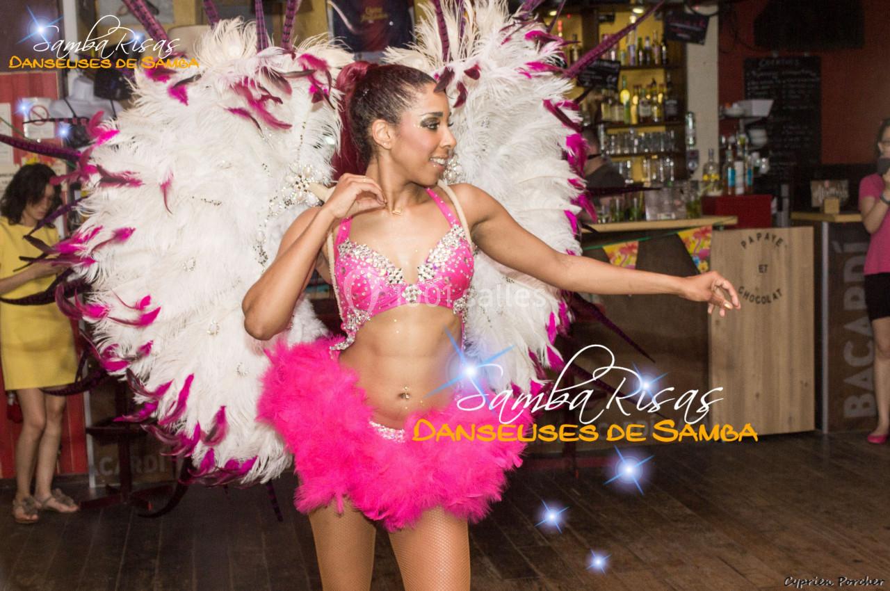 Danseuse de samba en tenue colorée avec plumes blanches, exécutant un mouvement dans un décor festif intérieur.