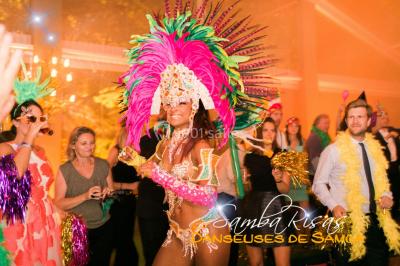 Trois hommes souriants en tenue de capoeira avec des drapeaux brésiliens, posant dans un parc ensoleillé.