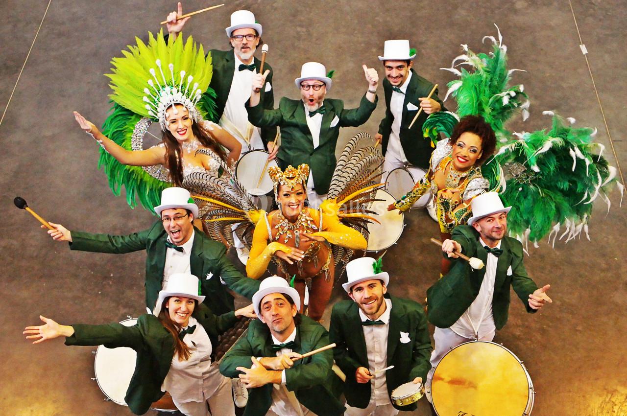 Groupe de musiciens et danseuses en costumes colorés et chapeaux, posant avec des instruments de percussion.