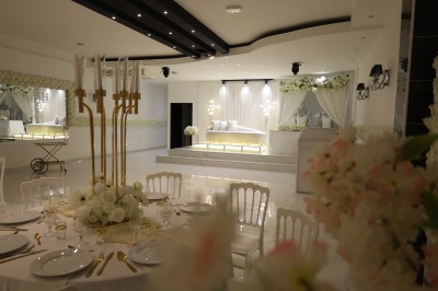 Salle lumineuse avec table drapée de blanc, décorée de fleurs et bougies, donnant sur un extérieur arboré.