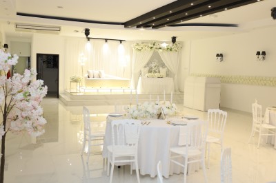 Salle lumineuse avec table drapée de blanc, décorée de fleurs et bougies, donnant sur un extérieur arboré.