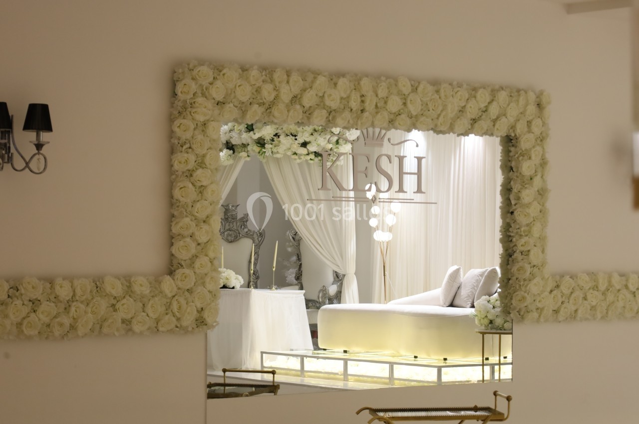 Grand miroir encadré de roses blanches reflétant un salon élégant avec canapé clair et décorations lumineuses.