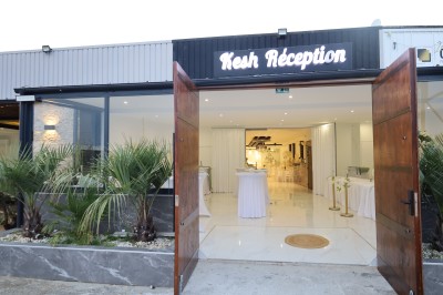Salle lumineuse avec table drapée de blanc, décorée de fleurs et bougies, donnant sur un extérieur arboré.
