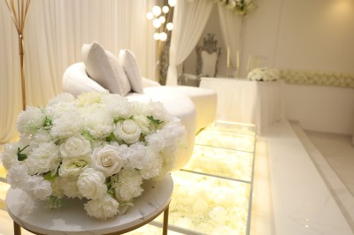 Salle lumineuse avec table drapée de blanc, décorée de fleurs et bougies, donnant sur un extérieur arboré.