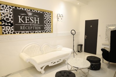 Salle lumineuse avec table drapée de blanc, décorée de fleurs et bougies, donnant sur un extérieur arboré.