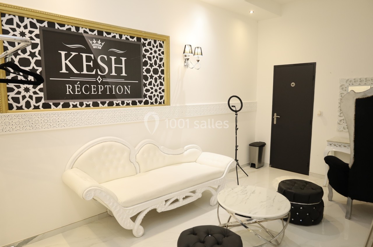 Salon lumineux avec canapé blanc, table basse, poufs noirs et panneau mural indiquant ’Kesh Réception’.