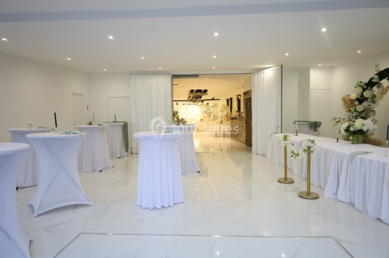 Salle de réception lumineuse avec tables hautes drapées de blanc et décorations florales élégantes.