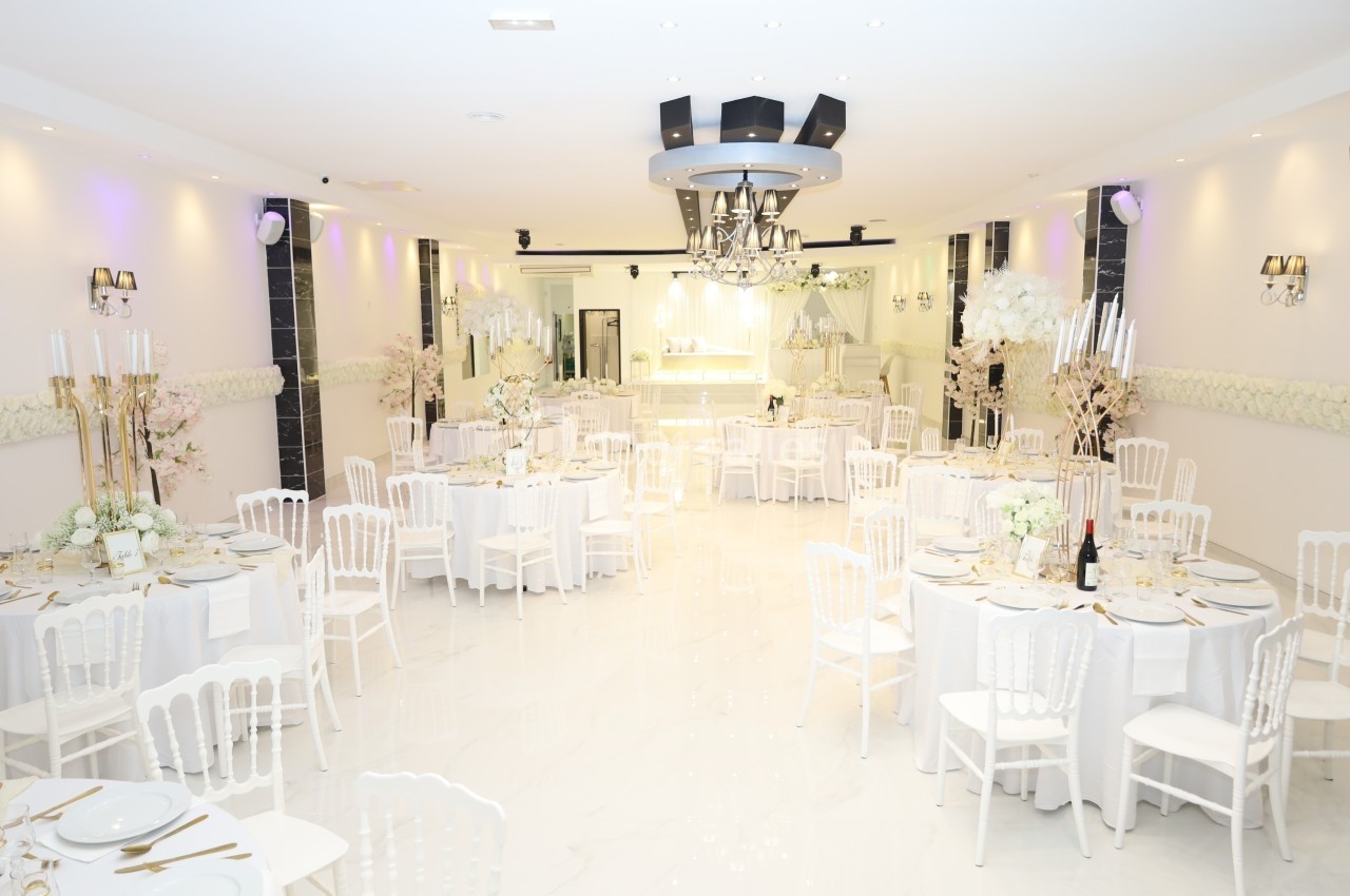 Salle de réception lumineuse avec tables rondes décorées de fleurs blanches et chaises blanches élégantes.