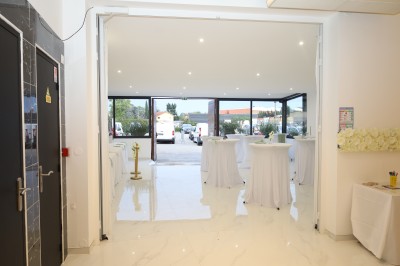 Salle lumineuse avec table drapée de blanc, décorée de fleurs et bougies, donnant sur un extérieur arboré.