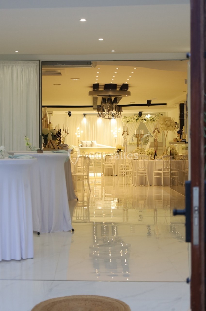 Salle de réception élégante avec tables dressées, décorations blanches et éclairage chaleureux.