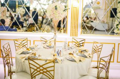 Table dressée avec une assiette blanche, un cadeau doré, une serviette beige nouée et des macarons en décoration.