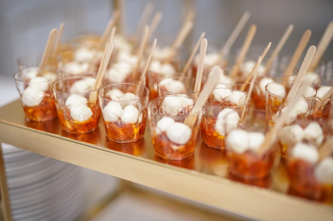 Verrines contenant des billes de mozzarella, tomates et cuillères en bois, disposées sur un présentoir doré.