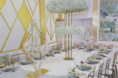 Table dressée avec une assiette blanche, un cadeau doré, une serviette beige nouée et des macarons en décoration.