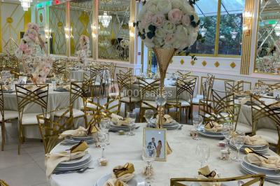 Table dressée avec une assiette blanche, un cadeau doré, une serviette beige nouée et des macarons en décoration.