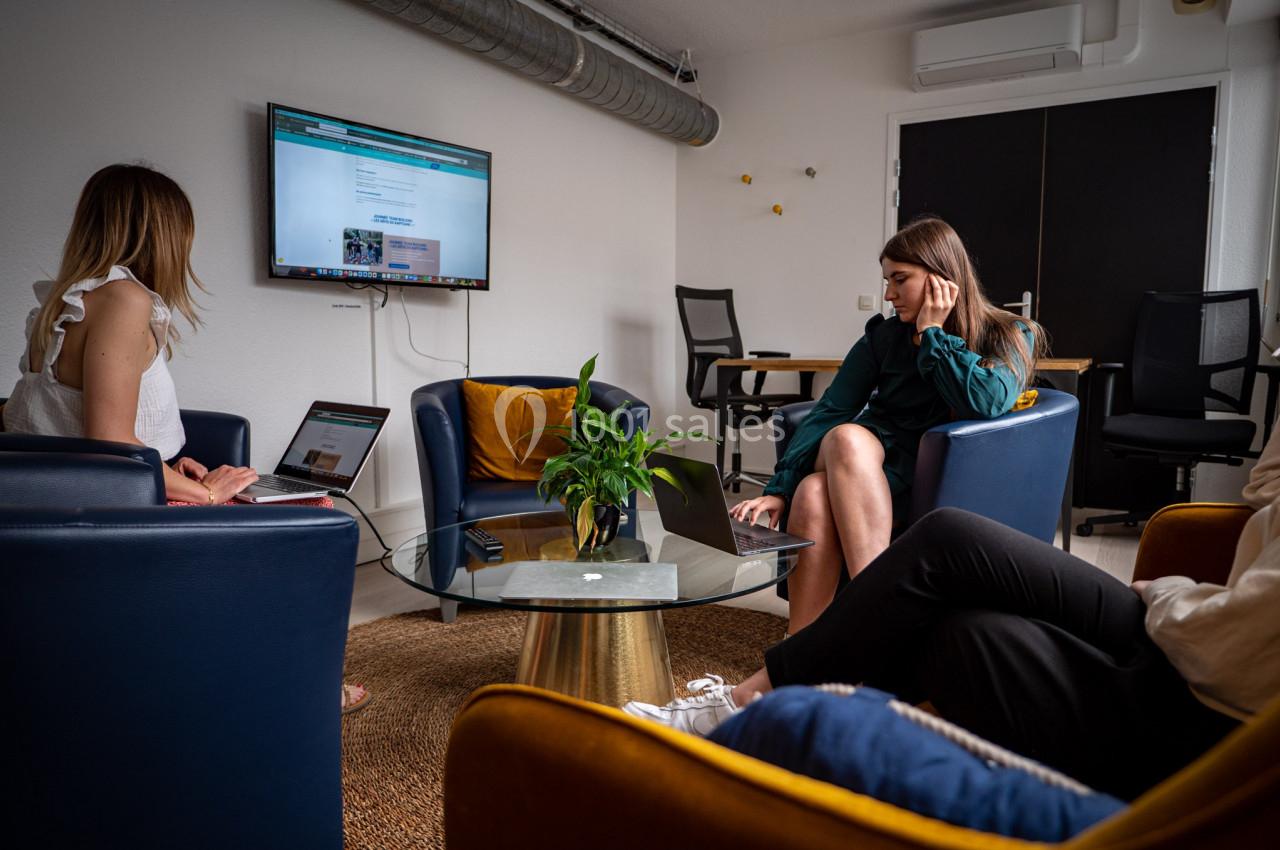 Trois personnes travaillent sur des ordinateurs portables dans une salle de réunion moderne avec un écran mural.