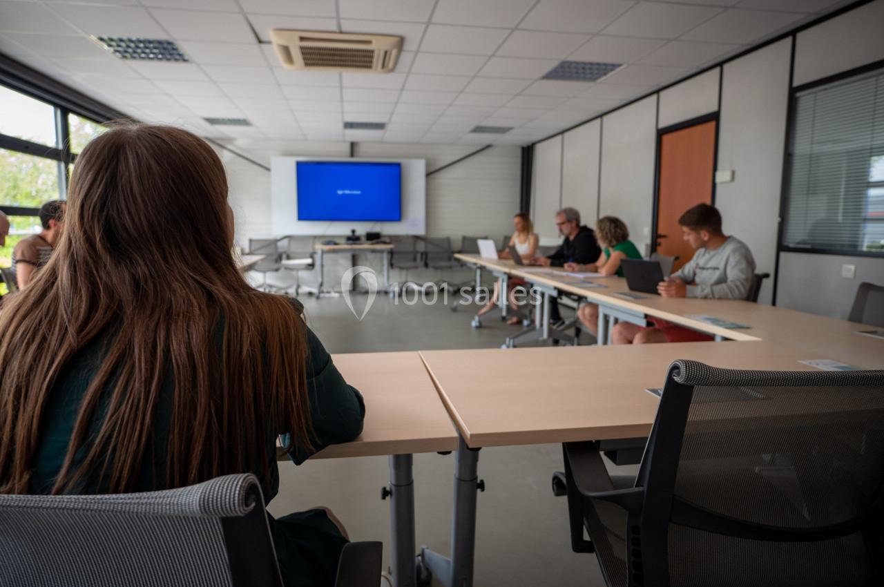 Personnes assises autour d'une table en salle de réunion, regardant un écran allumé affichant une page bleue.