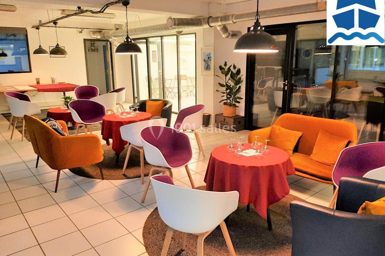 Salle lumineuse avec tables dressées, chaises colorées et décoration moderne, prête pour un repas ou une réunion conviviale.