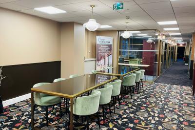 Salle moderne avec tables noires, chaises bleues, étagères murales, et écran mural dans un espace lumineux et décoré.