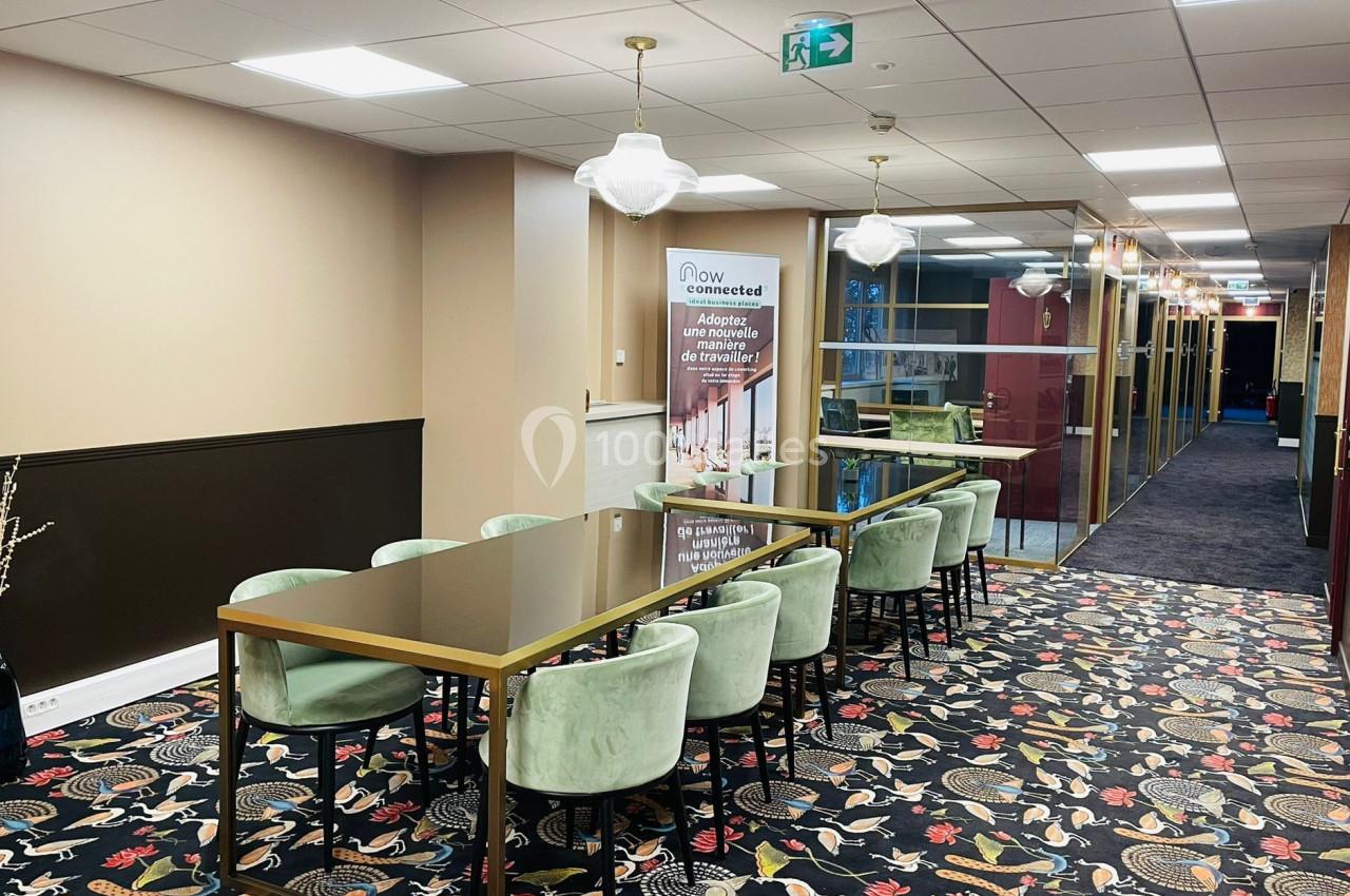 Salle de réunion moderne avec table en bois, chaises vertes, moquette colorée et éclairage suspendu.