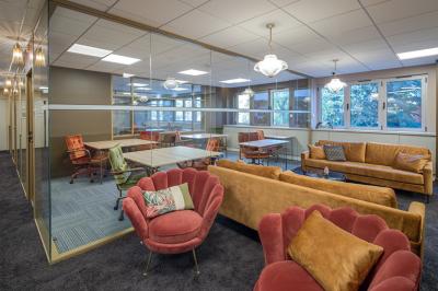 Salle moderne avec tables noires, chaises bleues, étagères murales, et écran mural dans un espace lumineux et décoré.