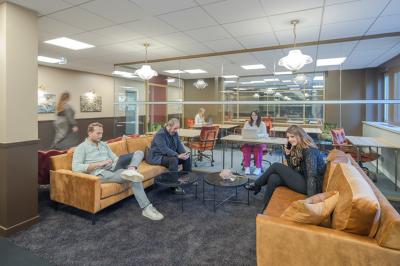 Salle moderne avec tables noires, chaises bleues, étagères murales, et écran mural dans un espace lumineux et décoré.