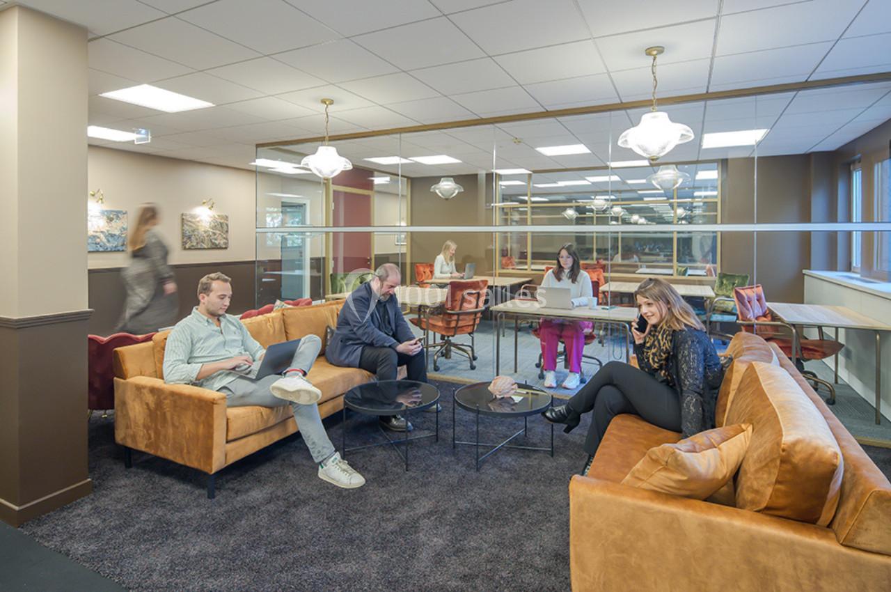 Personnes assises dans un espace de coworking lumineux, avec canapés, tables basses et bureaux en arrière-plan.